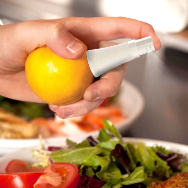 Hand holding a yellow lemon fitted with a white citrus sprayer over a salad